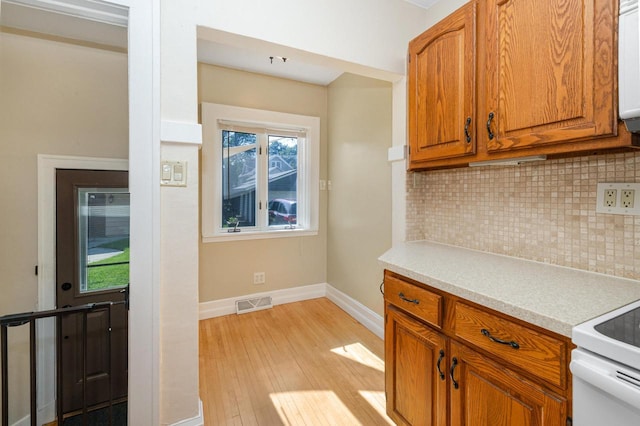 1441 N 66th St, Wauwatosa, WI 53213 - kitchen with light wood-style floors, decorative backsplash, light countertops, brown cabinetry, and white range with electric stovetop