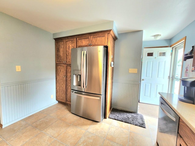 1239 Columbus Ave, Sheboygan, WI 53083 - kitchen featuring stainless steel appliances, a wainscoted wall, light countertops, brown cabinetry, and light tile patterned floors