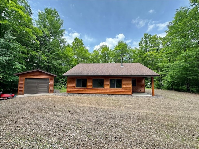 4686 W Butler Rd, Winter, WI 54896 - view of front facade with log veneer siding, an outbuilding, gravel driveway, a garage, and a shingled roof
