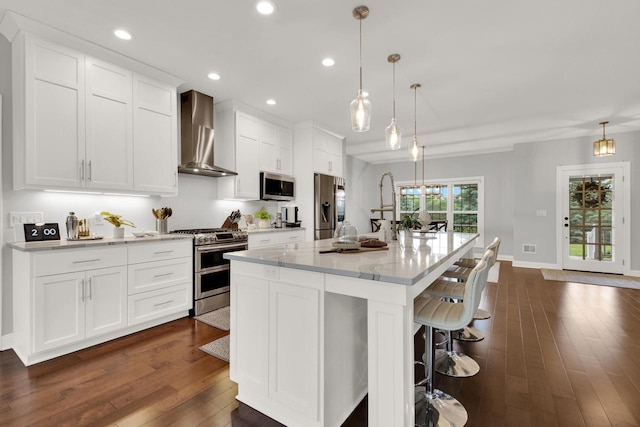 742 Charolais Dr, Slinger, WI 53086 - kitchen featuring stainless steel appliances, wall chimney range hood, dark wood-type flooring, white cabinets, and a center island with sink