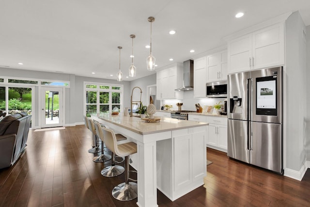 742 Charolais Dr, Slinger, WI 53086 - kitchen featuring stainless steel appliances, wall chimney range hood, light countertops, dark wood finished floors, and an island with sink