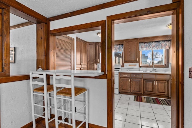 2963 Sunset Point Ln, Oshkosh, WI 54904 - kitchen featuring a kitchen breakfast bar, gas range gas stove, light tile patterned floors, brown cabinetry, and a textured ceiling