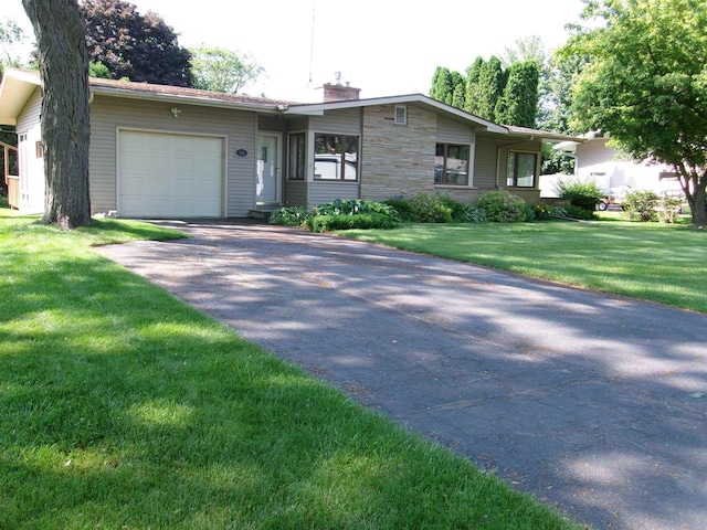 116 Mohawk Dr, Beaver Dam, WI 53916 - view of front facade featuring asphalt driveway, an attached garage, a chimney, a front yard, and stone siding