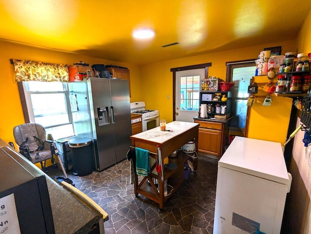 225 Caledonia St, La Crosse, WI 54603 - kitchen with gas range gas stove, refrigerator, brown cabinetry, and stainless steel fridge with ice dispenser