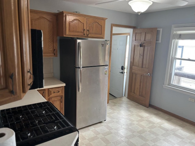 4945 W Tesch Ave, Milwaukee, WI 53220 - kitchen with freestanding refrigerator, gas stove, light countertops, light flooring, and brown cabinetry