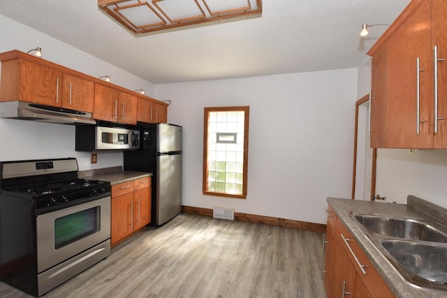 1600 Winslow St, Racine, WI 53404 - kitchen with stainless steel appliances, under cabinet range hood, brown cabinetry, light wood finished floors, and a textured ceiling