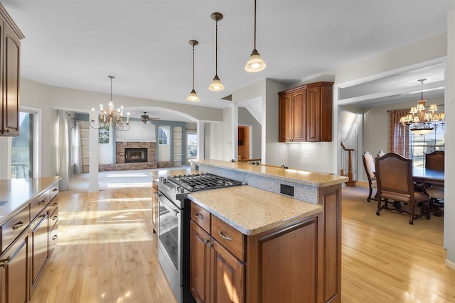 4227 Savannah Ct, Middleton, WI 53562 - kitchen featuring stainless steel gas stove, a chandelier, a brick fireplace, open floor plan, and light wood finished floors