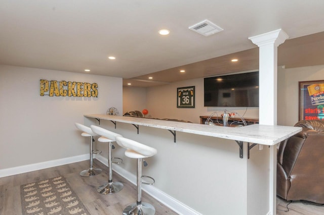 N69W29753 Ridgeview Ct, Hartland, WI 53029 - kitchen featuring recessed lighting, a kitchen breakfast bar, wood finished floors, light stone counters, and ornate columns