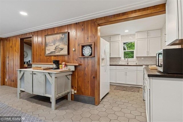 2818 Wilson Ave, Saint Croix Falls, WI 54024 - kitchen featuring black microwave, white fridge with ice dispenser, wood walls, white cabinets, and decorative backsplash