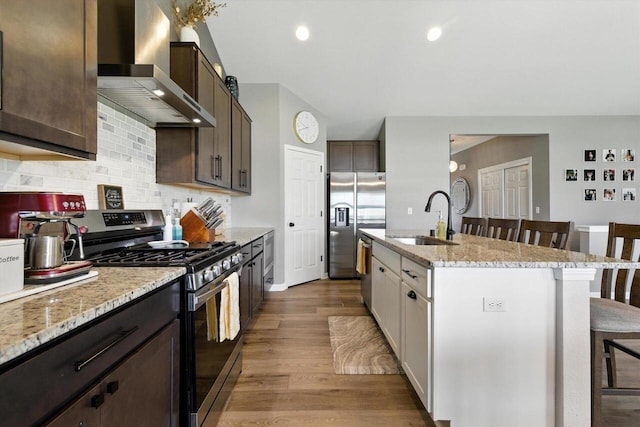 1143 Juniper Ln, Oconomowoc, WI 53066 - kitchen featuring appliances with stainless steel finishes, wall chimney range hood, a breakfast bar area, light wood-style floors, and dark brown cabinetry