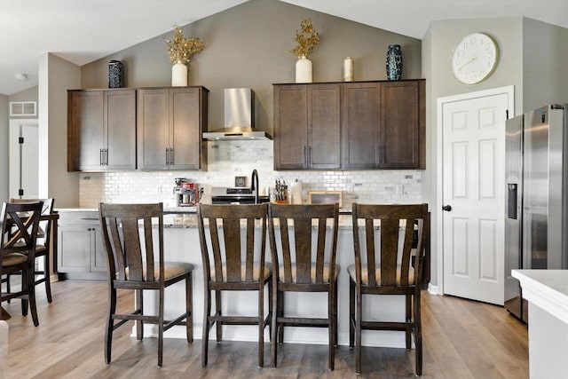 1143 Juniper Ln, Oconomowoc, WI 53066 - kitchen featuring stainless steel fridge with ice dispenser, wall chimney exhaust hood, vaulted ceiling, a breakfast bar, and light wood-style floors