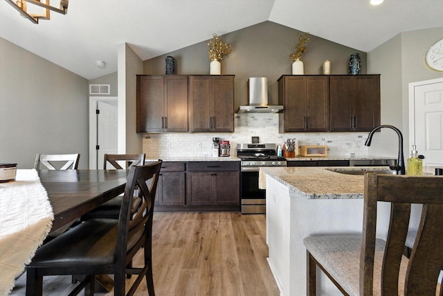 1143 Juniper Ln, Oconomowoc, WI 53066 - kitchen with stainless steel range with gas stovetop, wall chimney exhaust hood, lofted ceiling, light wood-style flooring, and dark brown cabinetry