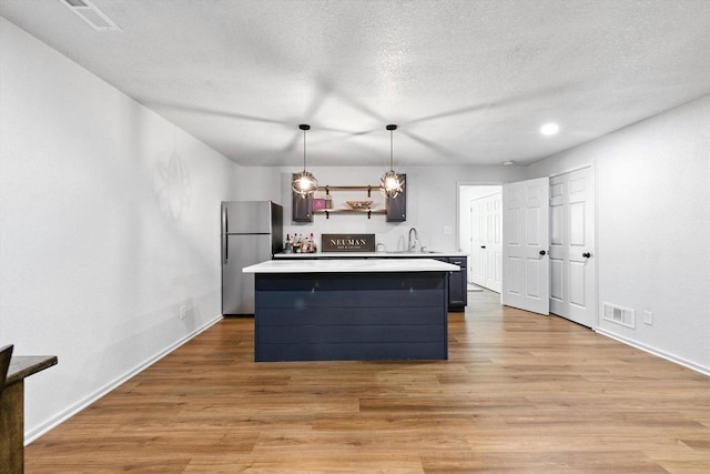 1143 Juniper Ln, Oconomowoc, WI 53066 - kitchen with freestanding refrigerator, light countertops, a kitchen island, light wood-style flooring, and pendant lighting