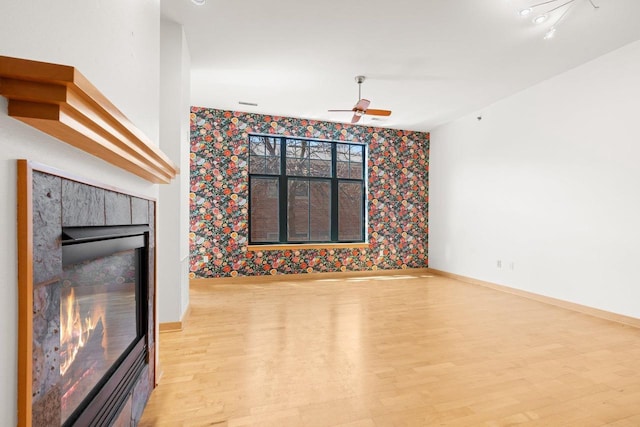 530 W Doty St Unit 107, Madison, WI 53703 - unfurnished living room featuring wallpapered walls, wood finished floors, ceiling fan, a tiled fireplace, and an accent wall