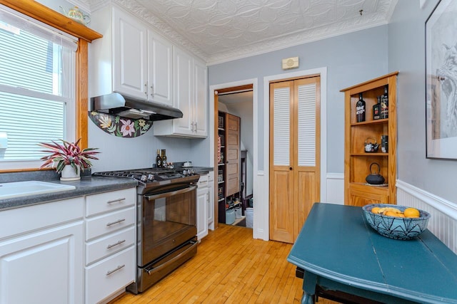 1756 Church St, Stevens Point, WI 54481 - kitchen with stainless steel gas range, under cabinet range hood, white cabinetry, light wood-style floors, and wainscoting