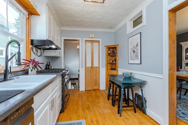 1756 Church St, Stevens Point, WI 54481 - kitchen with stainless steel gas range oven, light wood finished floors, under cabinet range hood, white cabinetry, and wainscoting