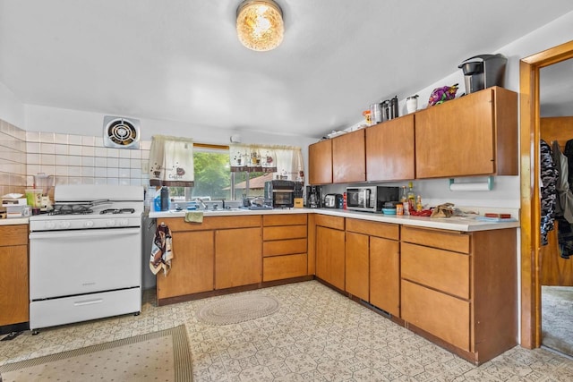 W914 Madsen Rd, Marinette, WI 54143 - kitchen with white range with gas cooktop, stainless steel microwave, light countertops, decorative backsplash, and brown cabinetry