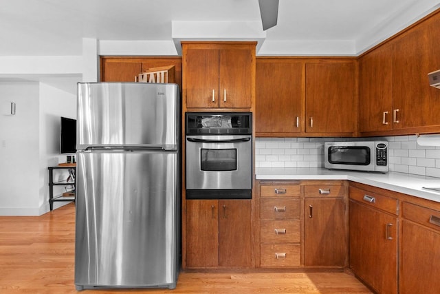 625 N Winnebago St, De Pere, WI 54115 - kitchen with appliances with stainless steel finishes, light countertops, backsplash, light wood-type flooring, and brown cabinetry