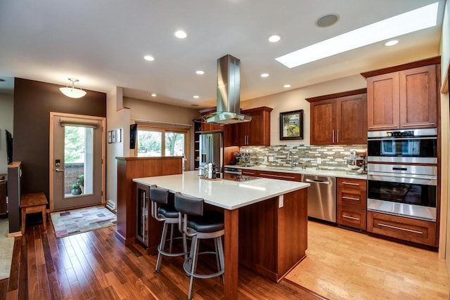 6846 Frank Lloyd Wright Ave, Middleton, WI 53562 - kitchen featuring stainless steel dishwasher, island exhaust hood, light countertops, light wood finished floors, and decorative backsplash