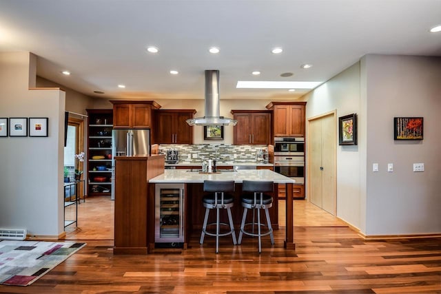 6846 Frank Lloyd Wright Ave, Middleton, WI 53562 - kitchen with wine cooler, appliances with stainless steel finishes, light wood finished floors, a kitchen island with sink, and decorative backsplash