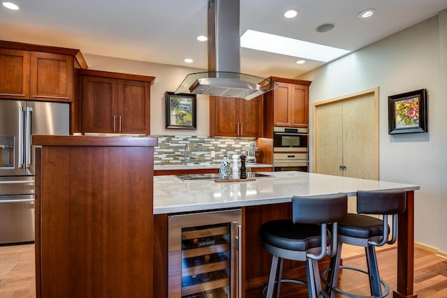 6846 Frank Lloyd Wright Ave, Middleton, WI 53562 - kitchen featuring beverage cooler, island exhaust hood, stainless steel appliances, a kitchen breakfast bar, and tasteful backsplash