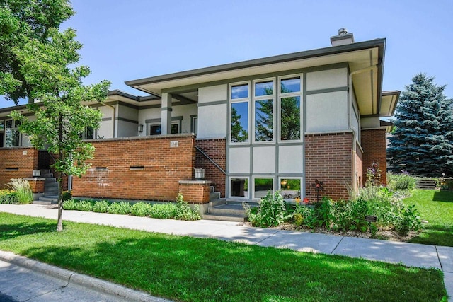 6846 Frank Lloyd Wright Ave, Middleton, WI 53562 - view of front of home featuring stucco siding, brick siding, a chimney, and a front yard