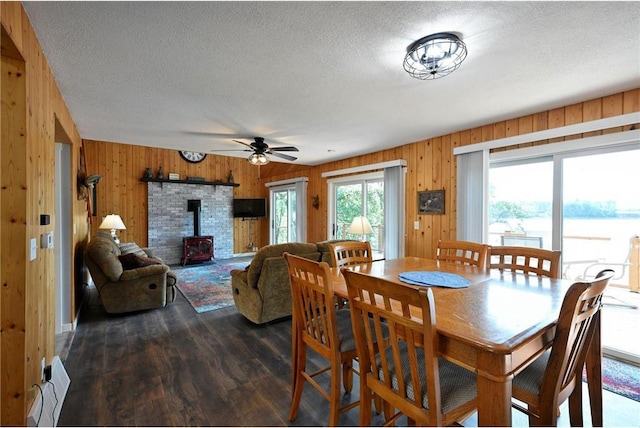 33516 No Mans Trl, Minong, WI 54859 - dining area with a wood stove, ceiling fan, wood walls, a textured ceiling, and dark wood-style flooring