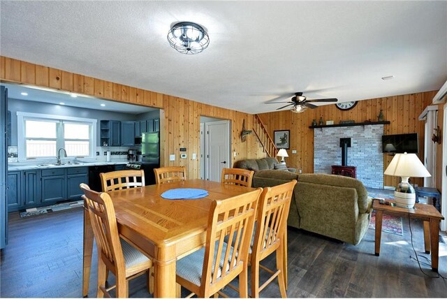 33516 No Mans Trl, Minong, WI 54859 - dining room with a wood stove, dark wood finished floors, a ceiling fan, wood walls, and stairway