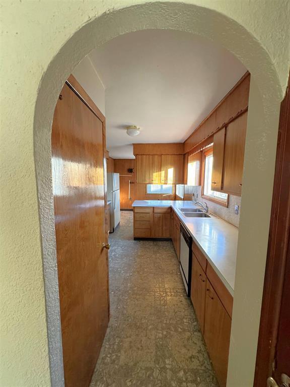 1117 21st St, Monroe, WI 53566 - kitchen featuring dishwasher, light countertops, freestanding refrigerator, a textured wall, and brown cabinets