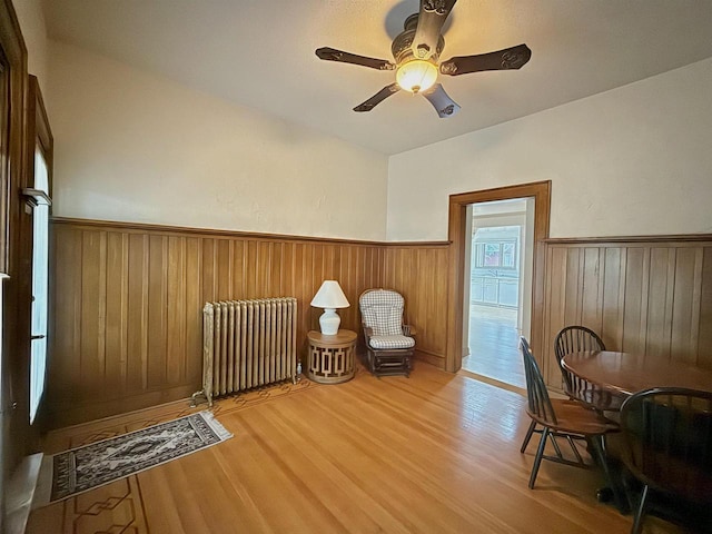 195 E Park Ave, Berlin, WI 54923 - living area featuring radiator heating unit, wainscoting, light wood-type flooring, a ceiling fan, and wood walls