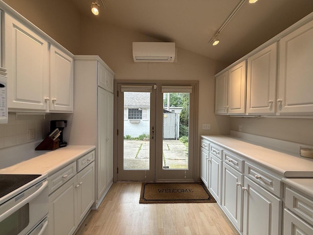 195 E Park Ave, Berlin, WI 54923 - kitchen featuring an AC wall unit, rail lighting, vaulted ceiling, white cabinetry, and light wood-style flooring