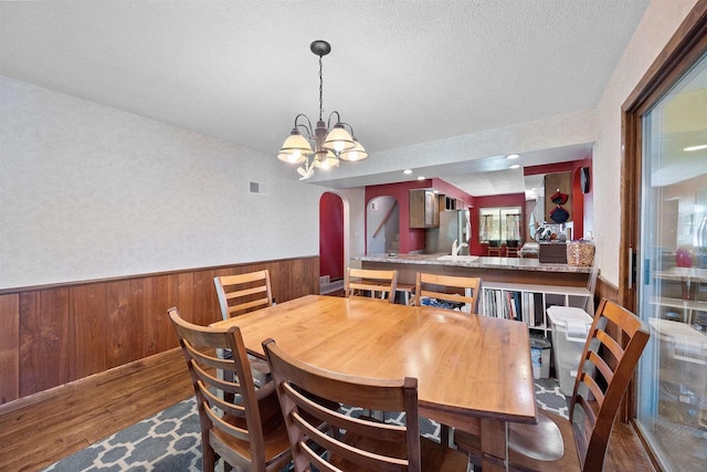 W4976 Pinewood Ln, Merrill, WI 54452 - dining area featuring wood finished floors, a chandelier, a wainscoted wall, wood walls, and arched walkways