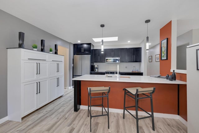 N78W15518 Old Gate Rd, Menomonee Falls, WI 53051 - kitchen with stainless steel appliances, a skylight, light wood-style flooring, decorative backsplash, and a peninsula
