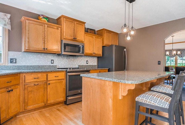 4474 N 107th St, Wauwatosa, WI 53225 - kitchen with appliances with stainless steel finishes, light wood-type flooring, backsplash, a kitchen breakfast bar, and a kitchen island