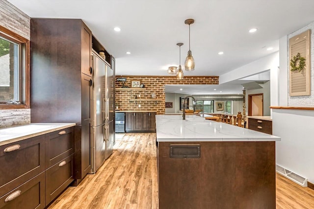 1450 Weber Ct, Hartland, WI 53029 - kitchen with light wood-style floors, decorative light fixtures, high end fridge, light stone counters, and dark brown cabinets