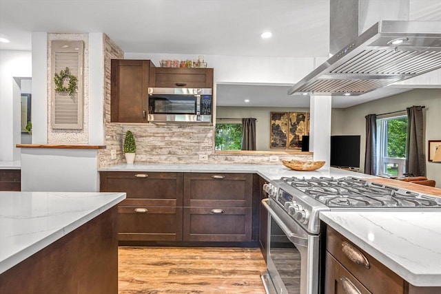 1450 Weber Ct, Hartland, WI 53029 - kitchen with wall chimney exhaust hood, appliances with stainless steel finishes, light stone counters, tasteful backsplash, and light wood-style flooring