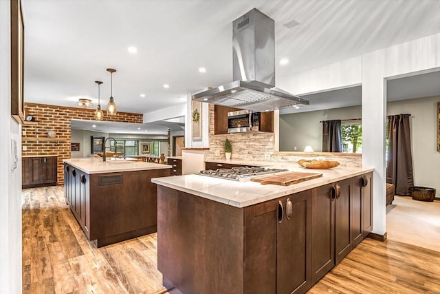 1450 Weber Ct, Hartland, WI 53029 - kitchen featuring island range hood, stainless steel appliances, a center island with sink, dark brown cabinetry, and light wood finished floors