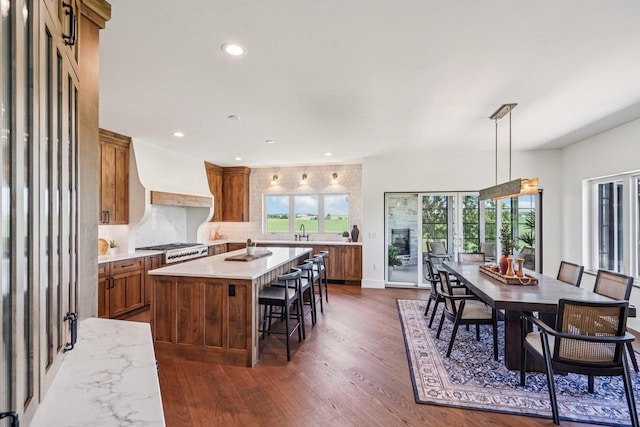 3330 Colton Way, Sun Prairie, WI 53590 - kitchen featuring brown cabinetry, premium range hood, light countertops, dark wood-style floors, and a kitchen bar