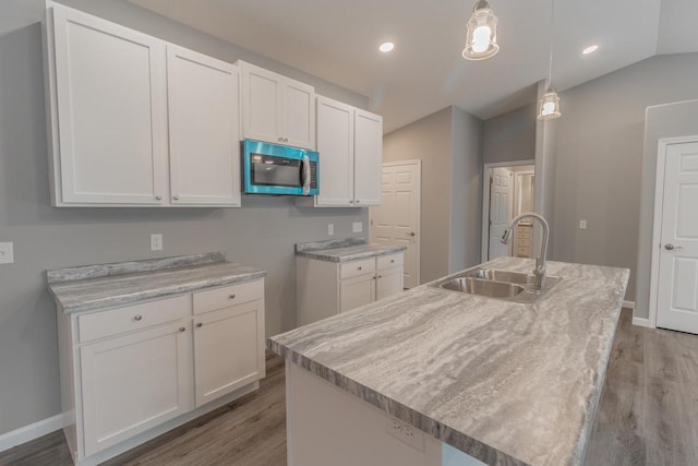 219 Joe St, Stevens Point, WI 54481 - kitchen with stainless steel microwave, light wood-style flooring, white cabinets, pendant lighting, and a kitchen island with sink