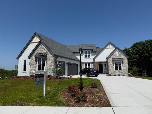 W214N6683 Fairview Dr, Menomonee Falls, WI 53051 - view of front of house with board and batten siding, stone siding, a garage, concrete driveway, and a front yard
