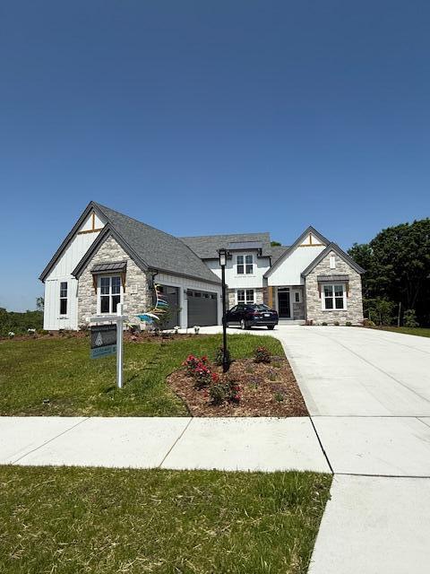 W214N6683 Fairview Dr, Menomonee Falls, WI 53051 - view of front of home featuring stone siding, concrete driveway, board and batten siding, a garage, and a front lawn
