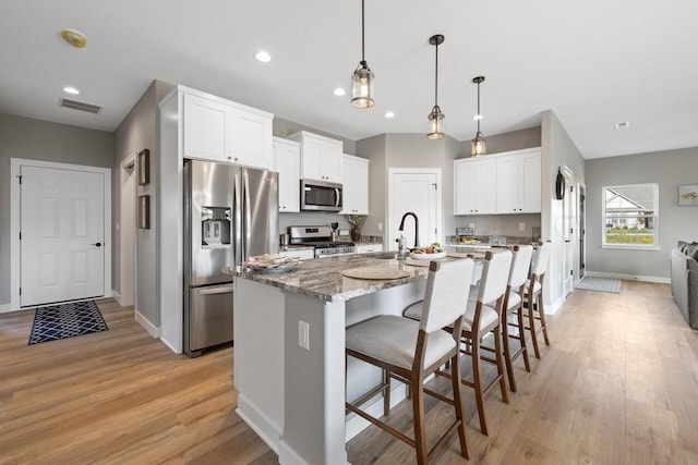 1883 Woodland Way, Slinger, WI 53086 - kitchen featuring stainless steel appliances, a breakfast bar, a center island with sink, light wood finished floors, and light stone countertops