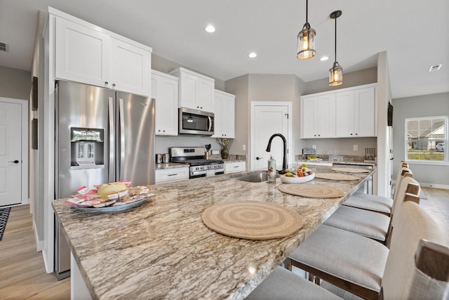 1883 Woodland Way, Slinger, WI 53086 - kitchen featuring appliances with stainless steel finishes, light wood-style flooring, a breakfast bar area, white cabinetry, and a spacious island