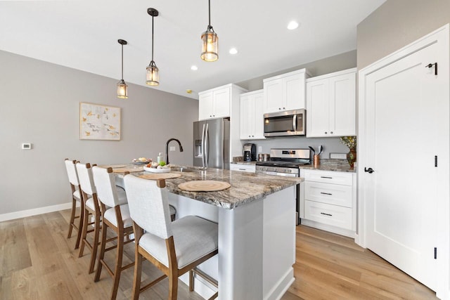 1883 Woodland Way, Slinger, WI 53086 - kitchen featuring appliances with stainless steel finishes, light wood-type flooring, a breakfast bar area, a center island with sink, and white cabinets