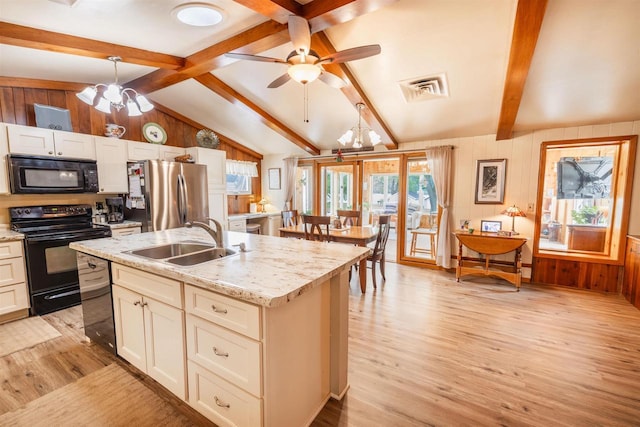 2278 S Riverside Dr, Beloit, WI 53511 - kitchen with black appliances, light wood-style flooring, a chandelier, wooden walls, and an island with sink
