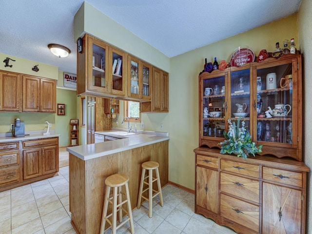 10811 S Patterson Rd, Solon Springs, WI 54873 - kitchen featuring a kitchen breakfast bar, brown cabinetry, glass insert cabinets, light countertops, and a textured ceiling