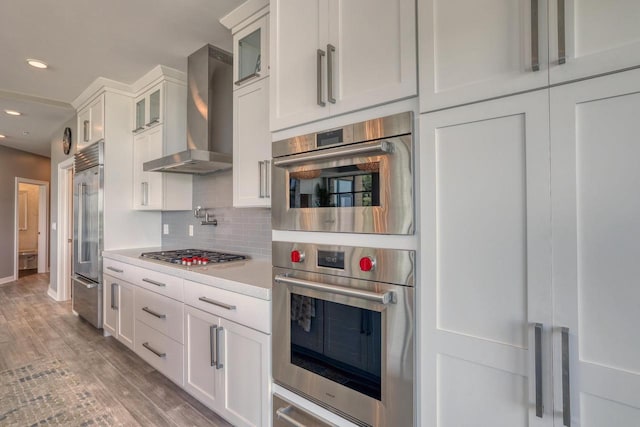 215 E Pleasant St Unit 304, Oconomowoc, WI 53066 - kitchen with wall chimney exhaust hood, stainless steel appliances, light countertops, white cabinetry, and glass insert cabinets