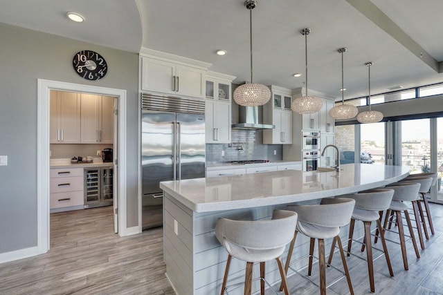 215 E Pleasant St Unit 304, Oconomowoc, WI 53066 - kitchen featuring appliances with stainless steel finishes, decorative backsplash, a large island with sink, white cabinets, and light wood-style floors