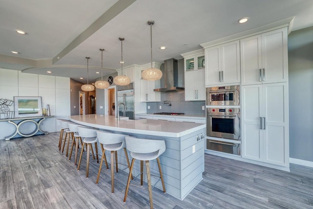 215 E Pleasant St Unit 304, Oconomowoc, WI 53066 - kitchen with wall chimney exhaust hood, a warming drawer, appliances with stainless steel finishes, light countertops, and light wood-type flooring