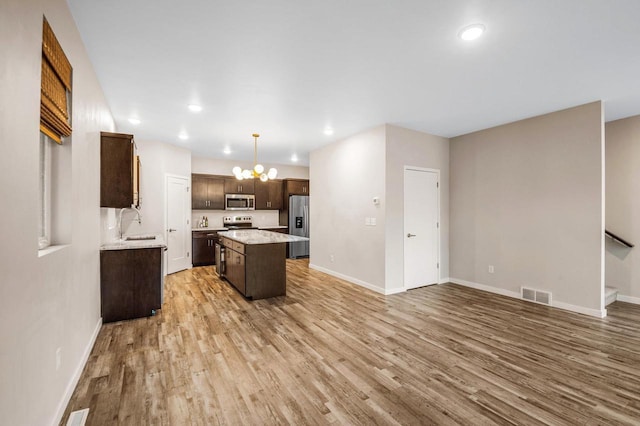 217 N Van Buren St, Green Bay, WI 54301 - kitchen with appliances with stainless steel finishes, light wood finished floors, a center island, dark brown cabinetry, and a chandelier